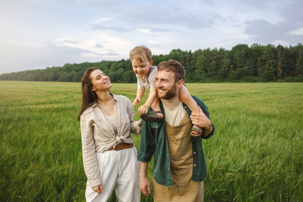 Eine Familie, Mutter, Vater, Kind, steht auf einer grünen Wiese.