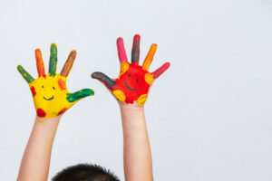 Hände eines Kindes, auf grauen Hintergrund, mit bunter Farbe verschmiert - Image by jcomp on Freepik